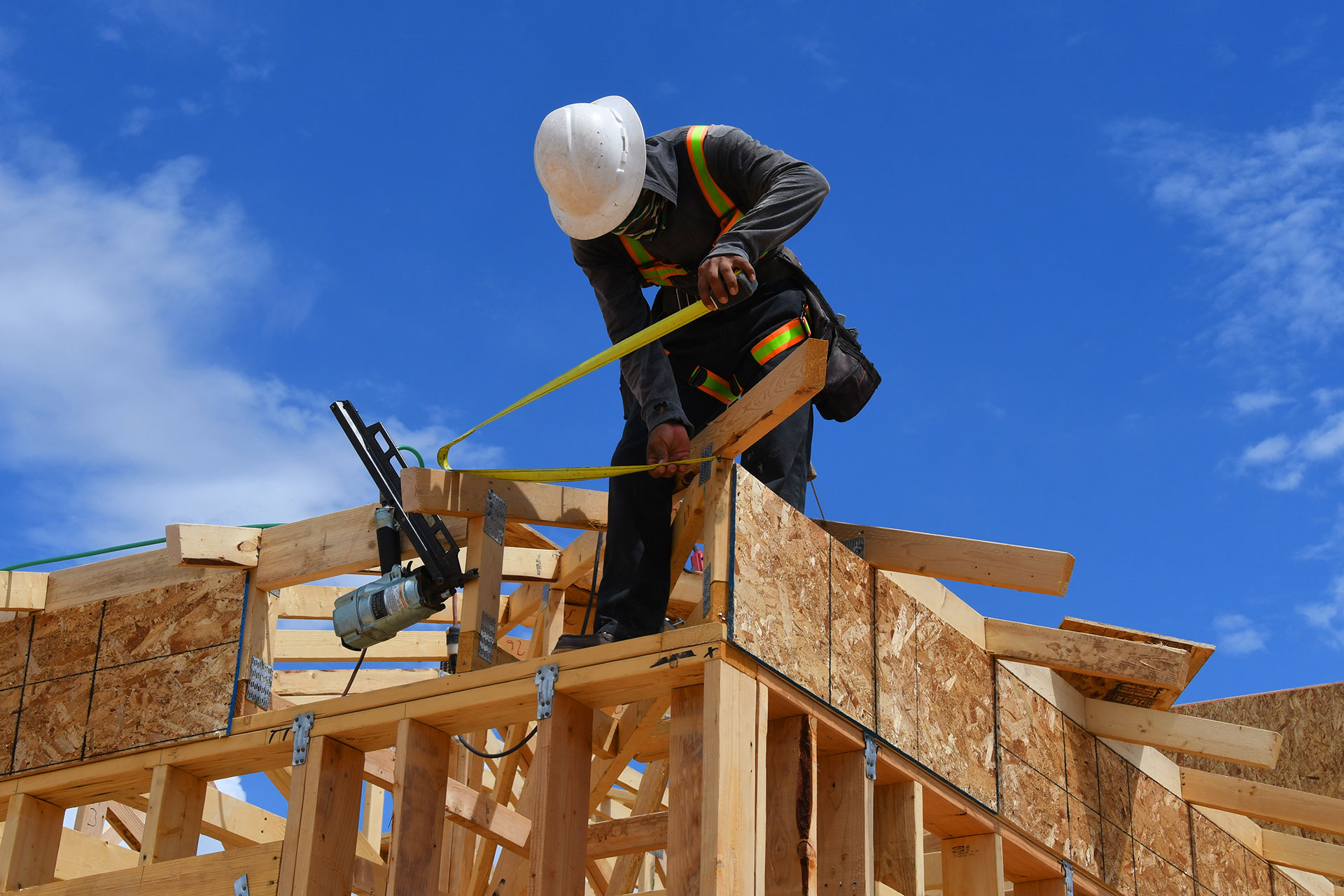 Construction worker measuring wood framing on residential roof structure